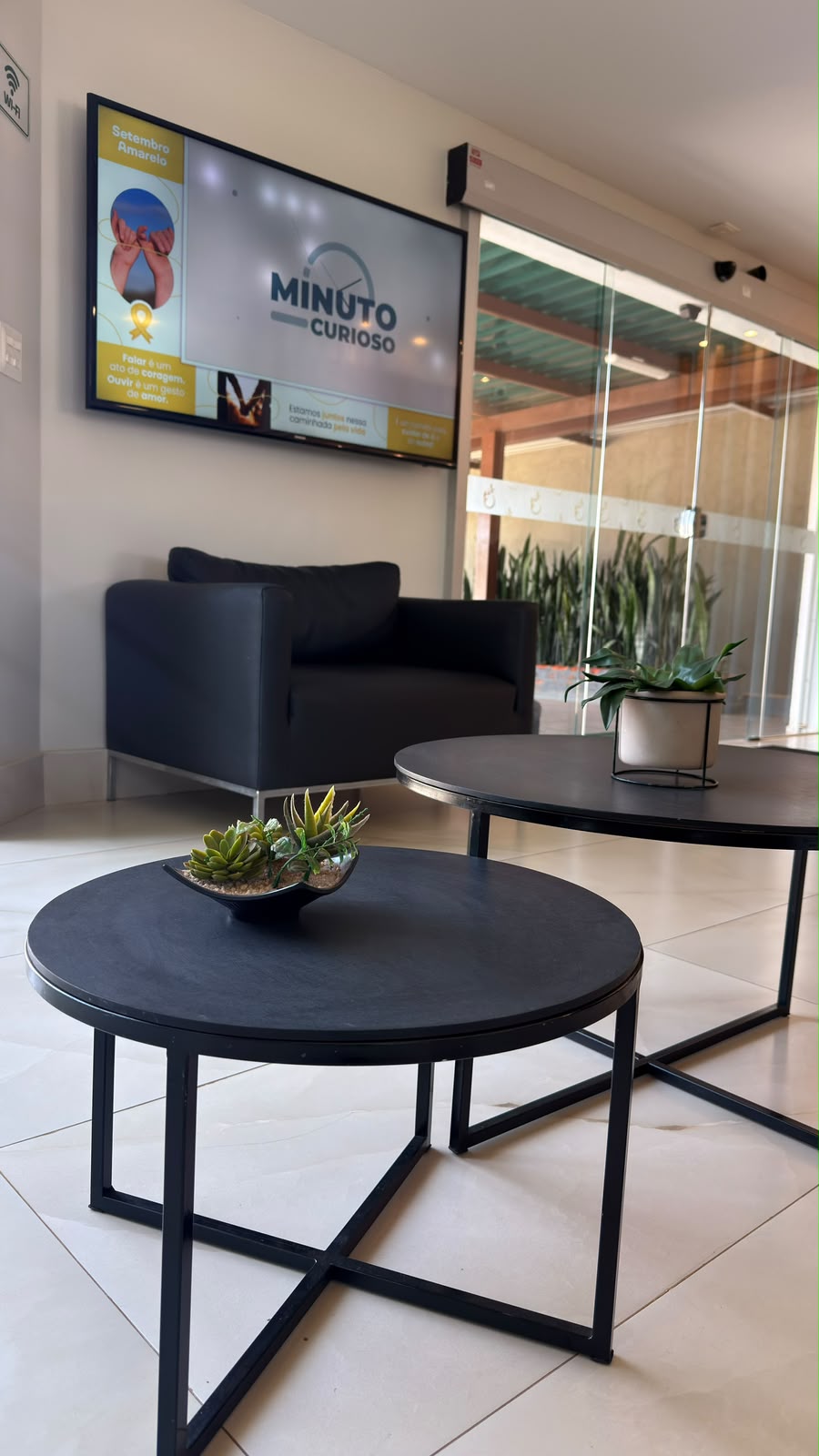 Sala de espera com poltronas, mesas de centro e televisão